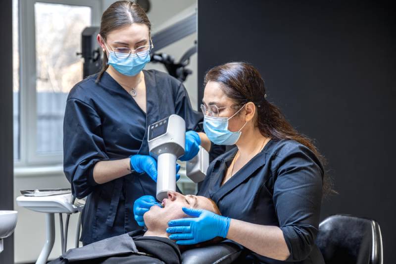 Dental assistant and dentist treating a patient with an intraoral X-ray in a modern dental practice