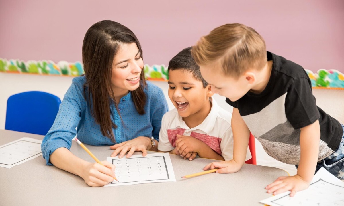 Lead teacher helping two young students with a counting worksheet in a bright classroom