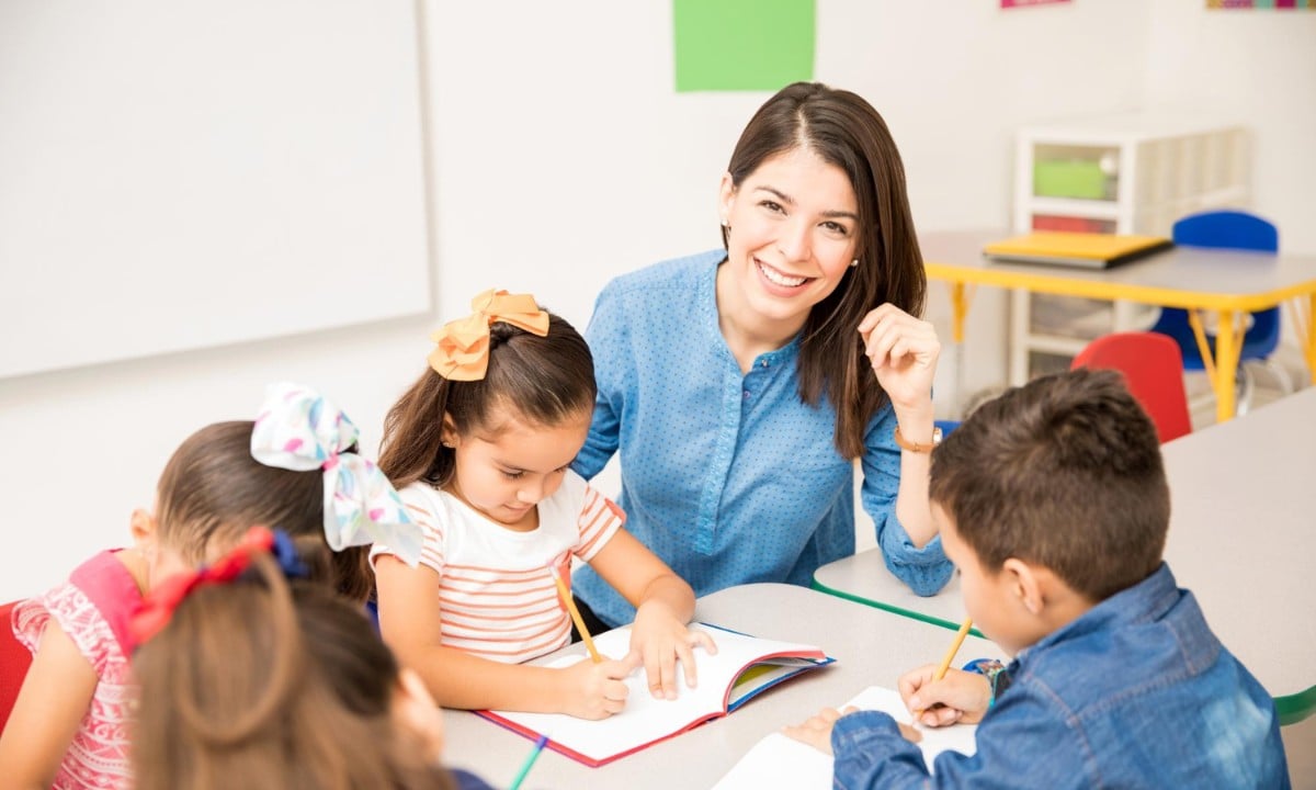 Substitute teacher smiling with a group of young students working at a classroom table